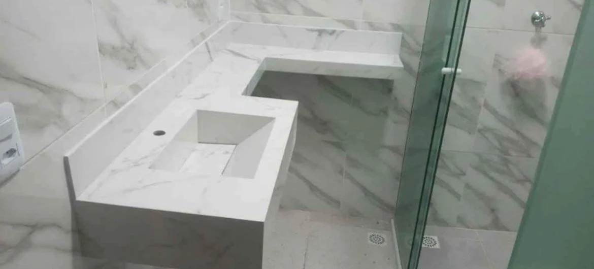 Lavatório branco com cuba esculpida e bancada junto ao box